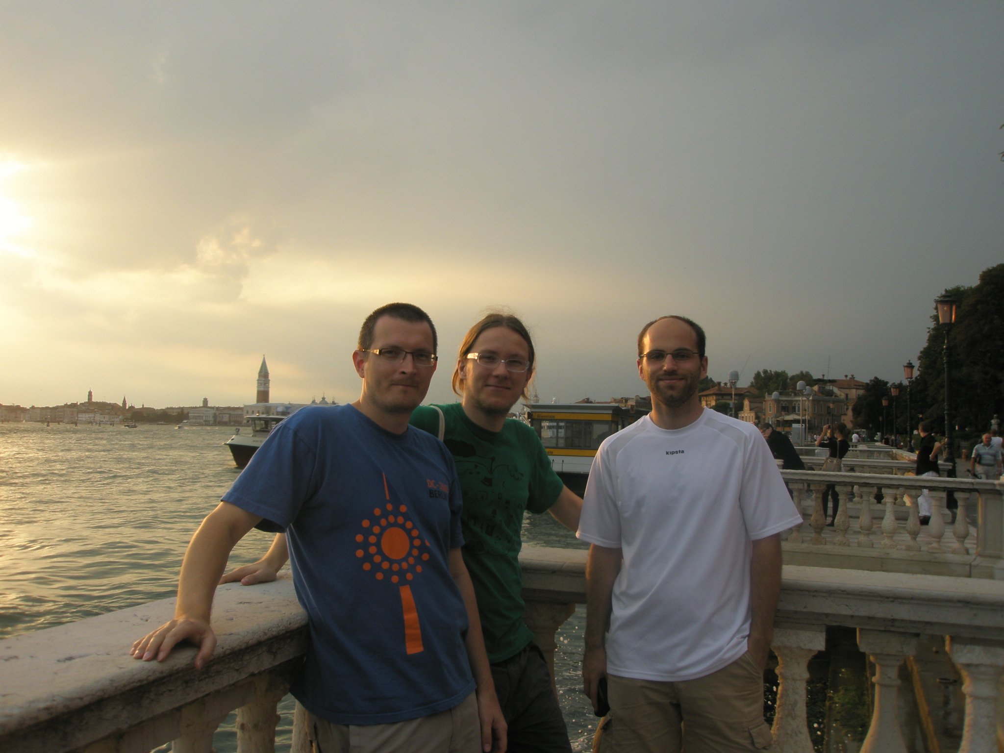three men pose together on a bridge near the water