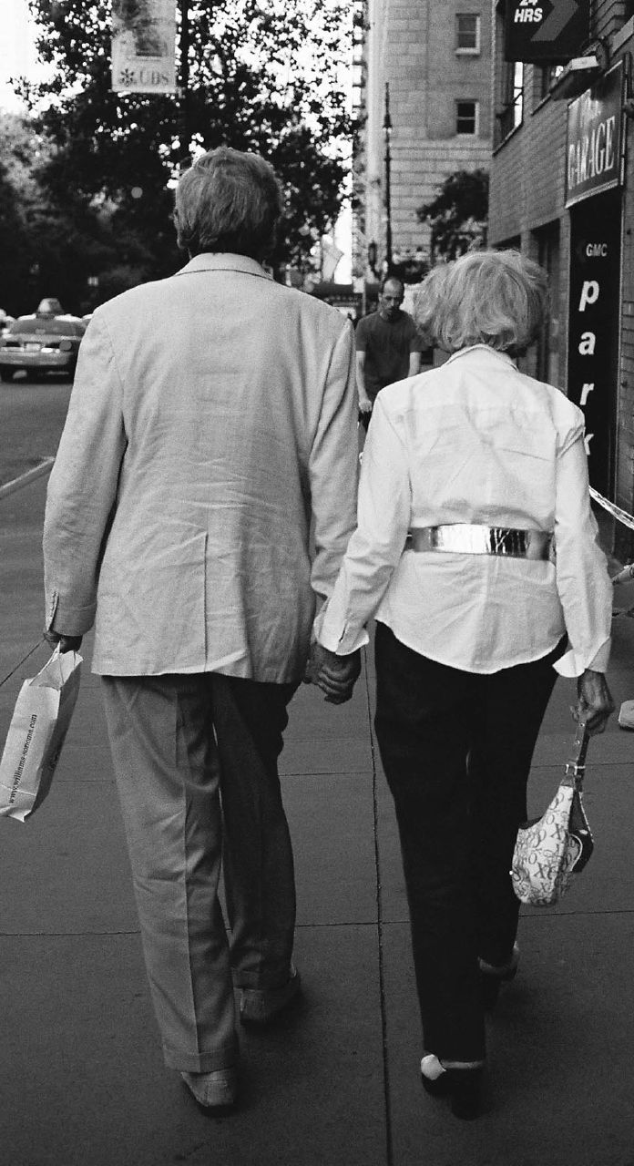 two older people walking down a street holding hands