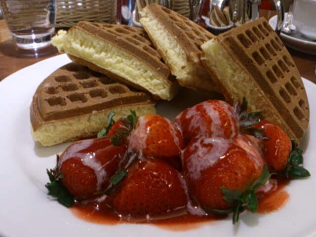 some strawberries on a white plate with waffles and syrup