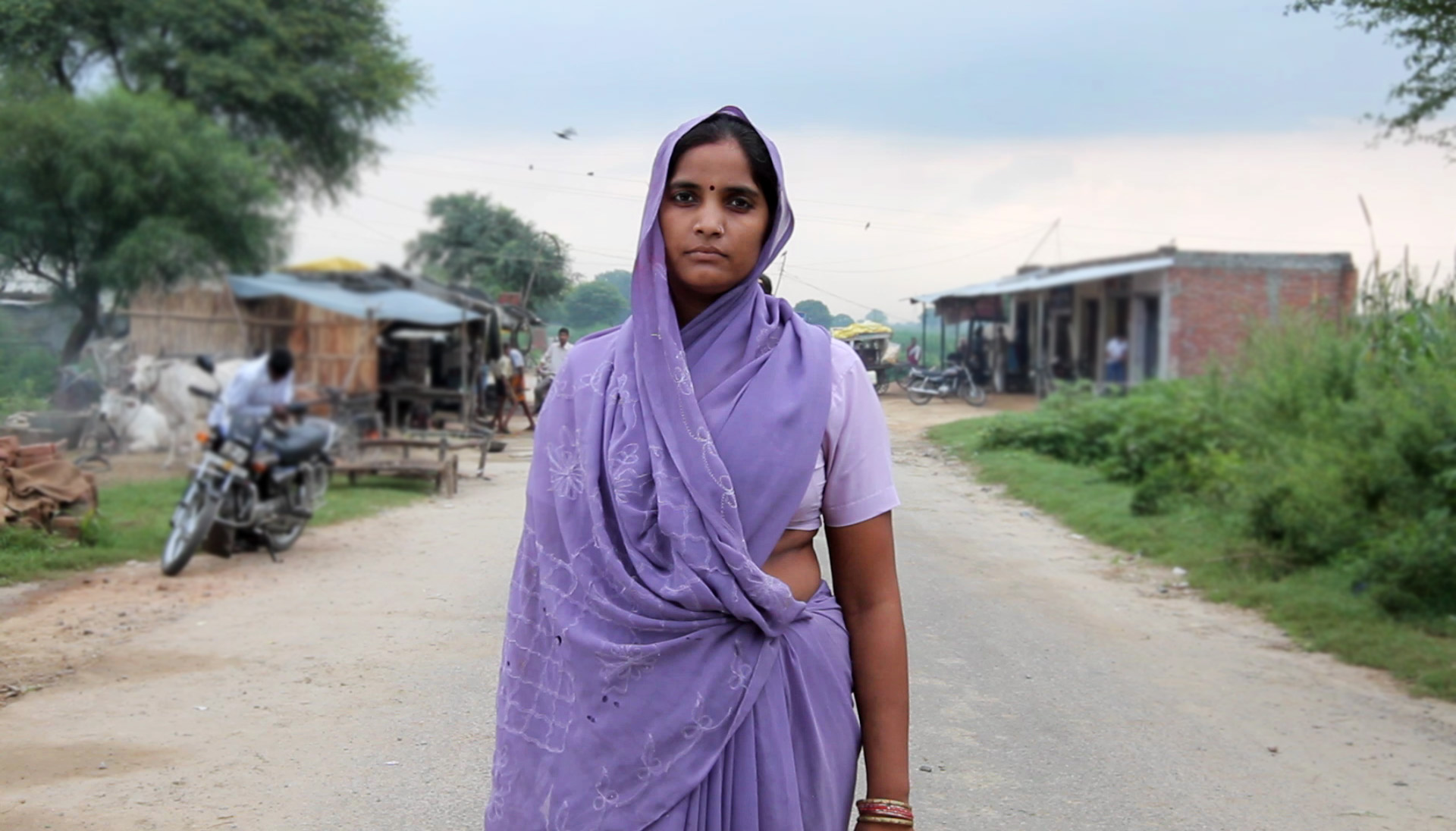 a woman standing on a dirt road wearing a purple gown