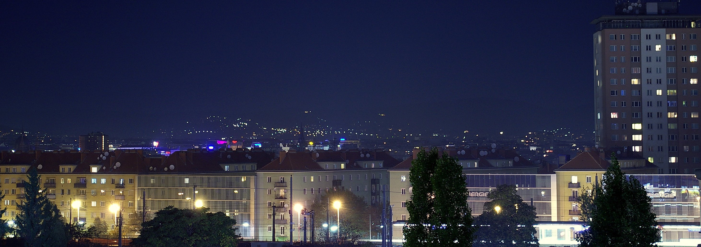 a city at night time is lit up and the lights of buildings glow in the distance