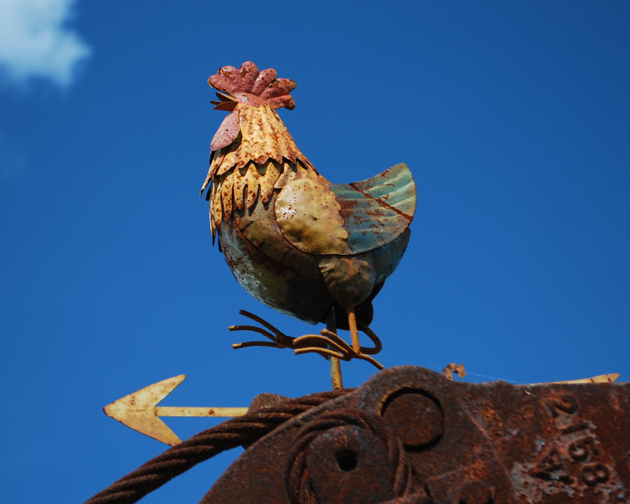 a rusty rooster perched on top of an old sign