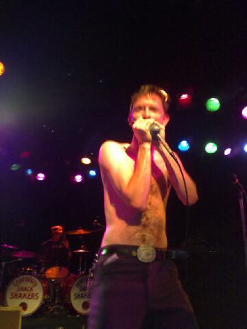 a man in shorts is shirtless while holding a microphone and singing into a microphone
