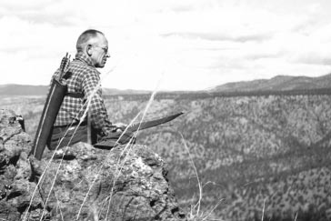 a man sitting on top of a cliff near a mountain