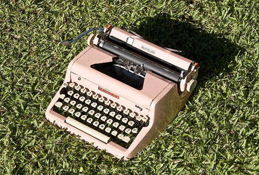 an old pink typewriter sitting in the grass