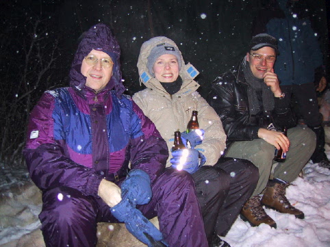 three men wearing cold weather attire sit in the snow