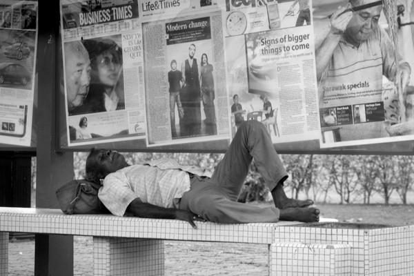 a man laying on top of a street sidewalk next to a newspaper