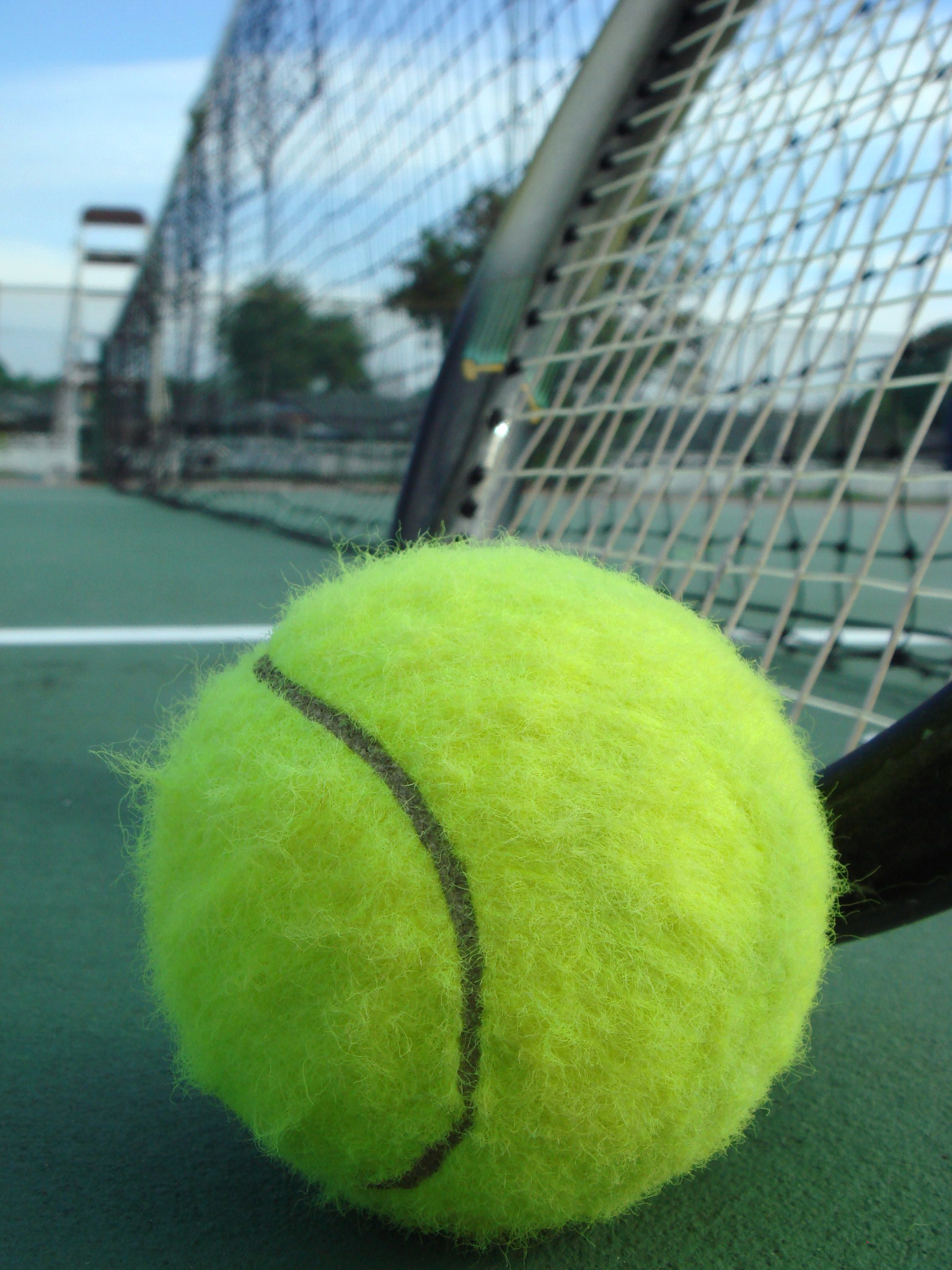 a yellow tennis ball with black stitching sitting on the edge of a net