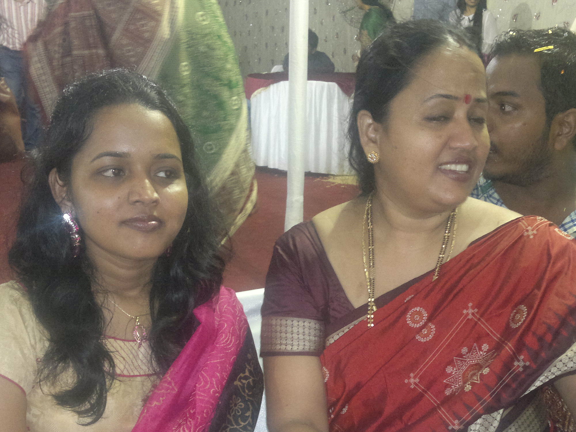 two women wearing traditional indian outfits sitting at a wedding