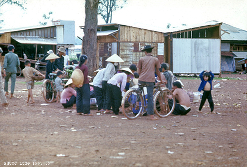 several people with a bike in the dirt and some people in a town