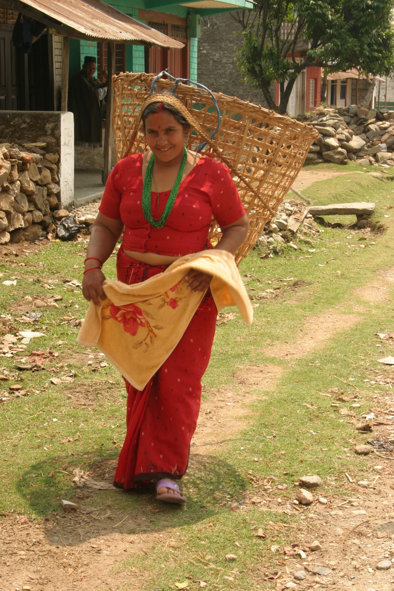 a woman carrying wickers walks on a dirt path