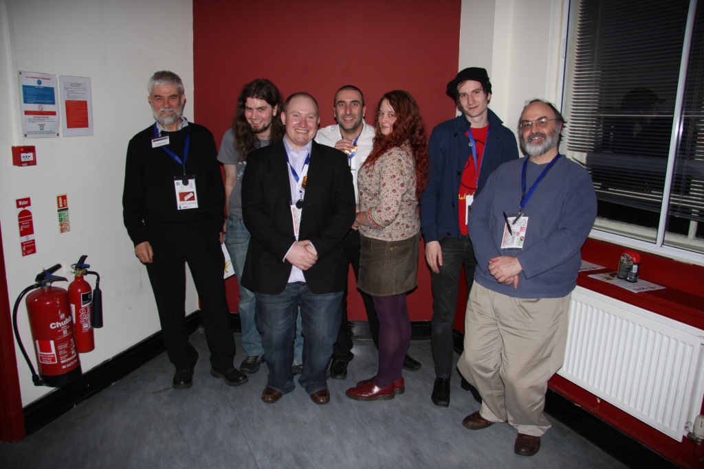 seven people pose in a room with red and white walls