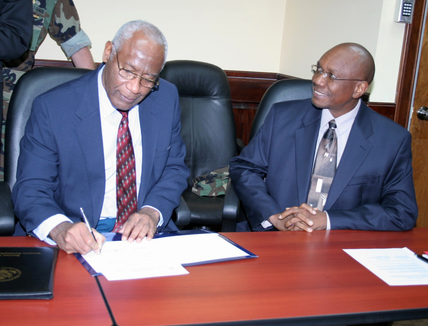 two african men seated at a conference table signing papers