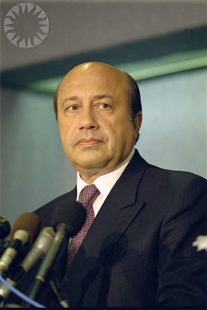 an asian man standing next to microphones and looking off to his right
