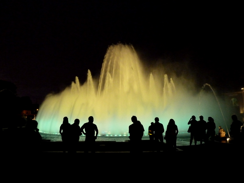 several people gather around a water fountain at night