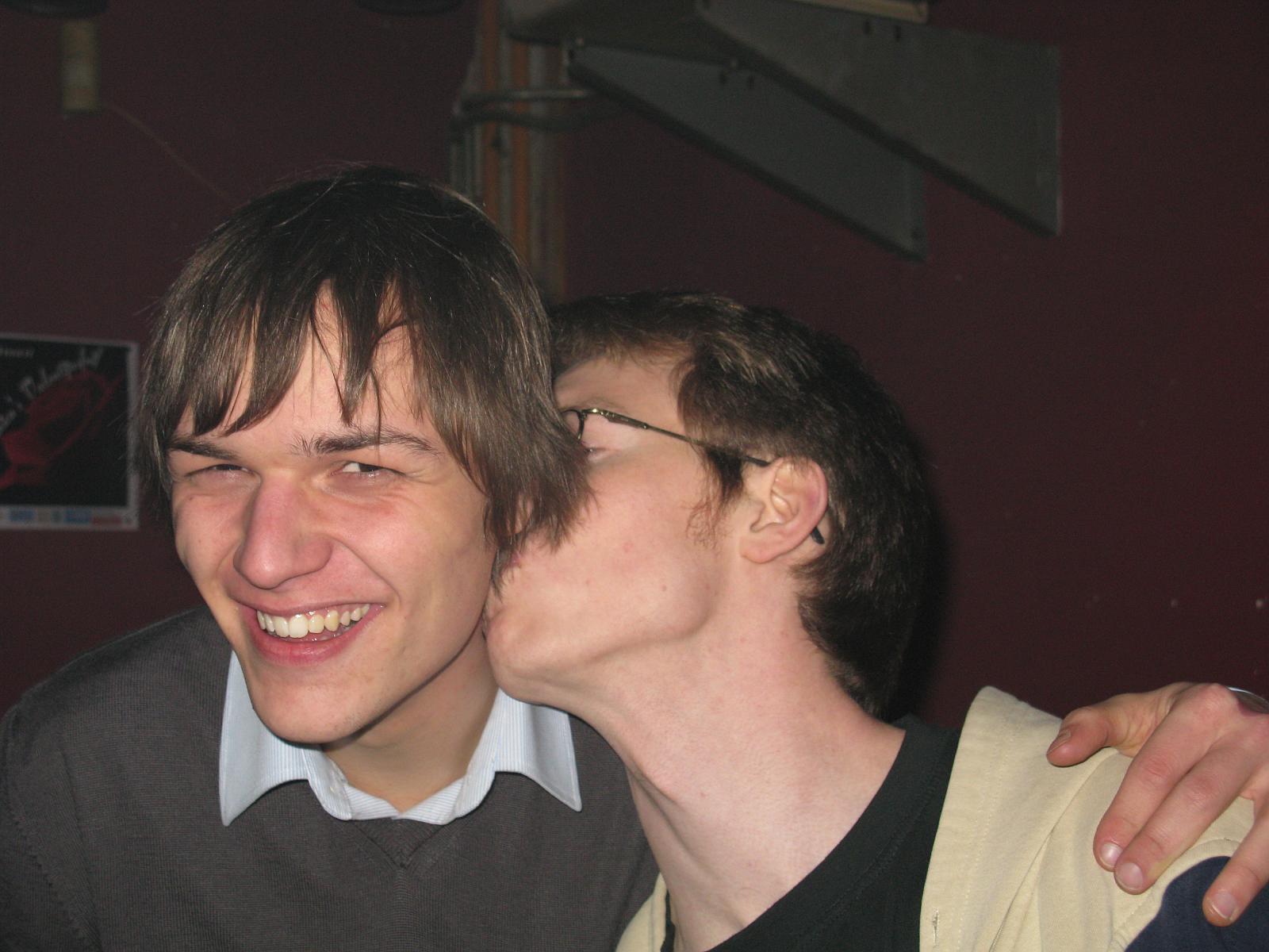two boys kissing and smiling together with one of them looking at the camera