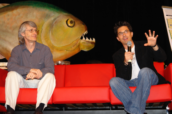two men sitting on a couch holding a microphone