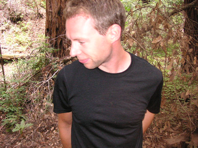 a man in black shirt in front of some trees