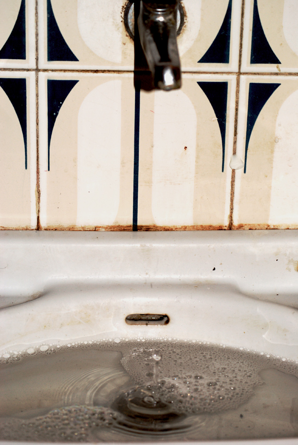 a dirty sink drain in front of a tiled wall