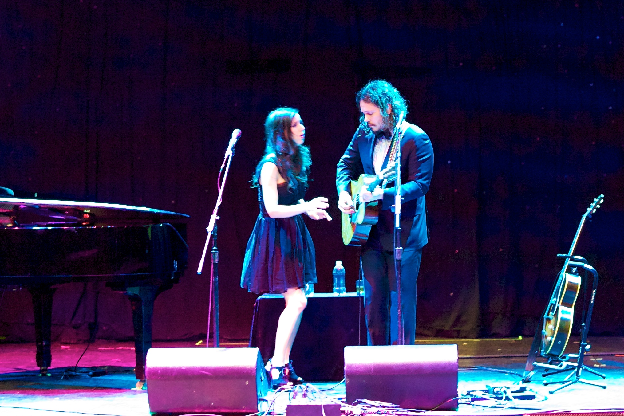 a man standing next to a woman with a guitar on a stage