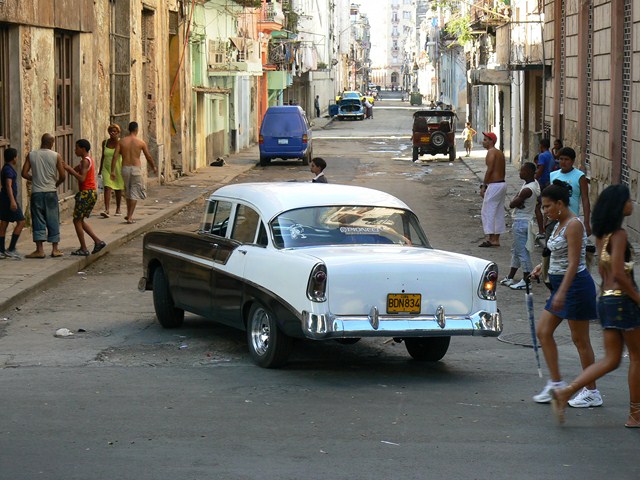 a street scene with an old car parked on the side of the road