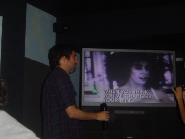 two people stand in front of a television while watching the screen