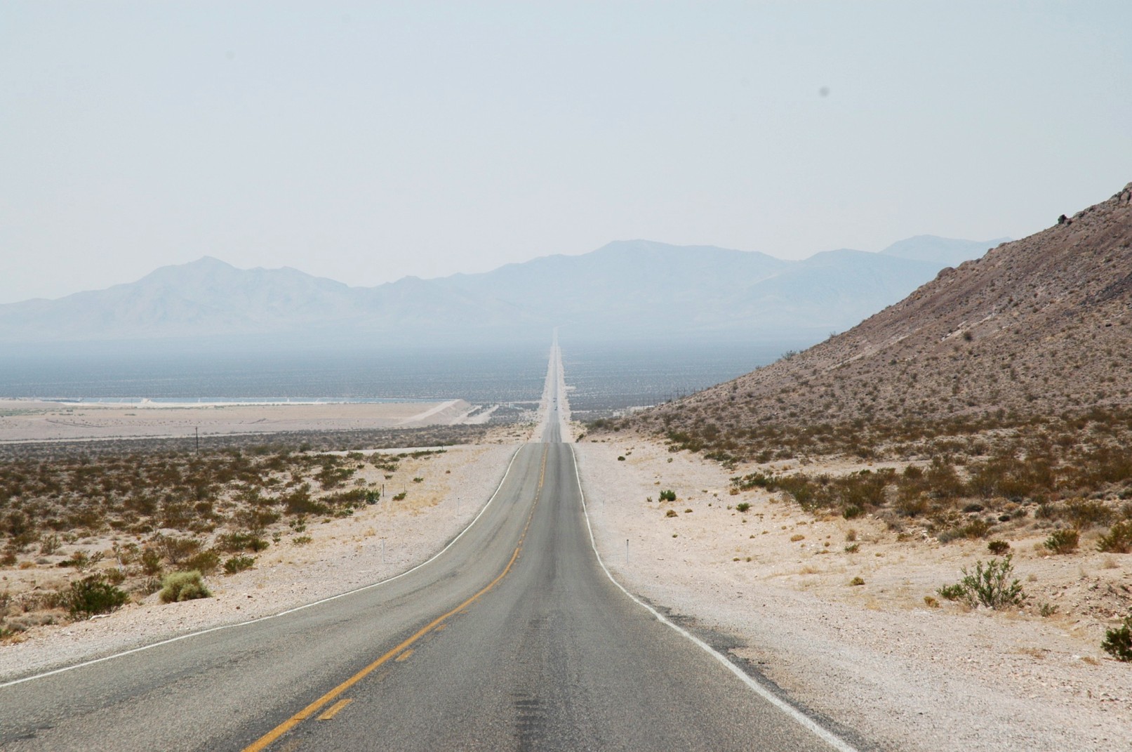 an empty road on the side of a desert with mountains in the distance