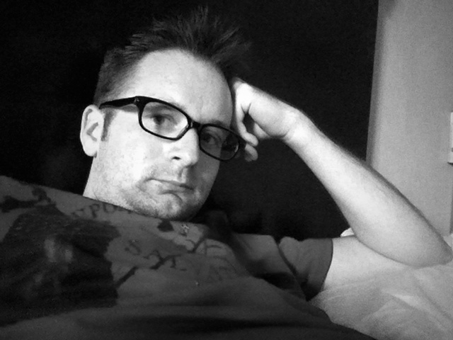 a black and white po of a man in glasses resting on a couch