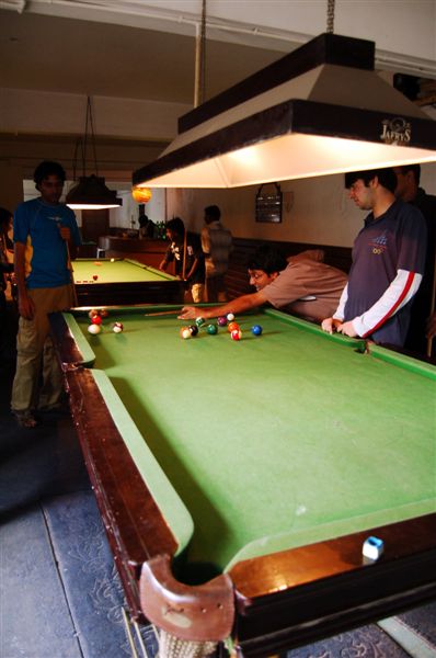 two men are playing pool with many other people standing around