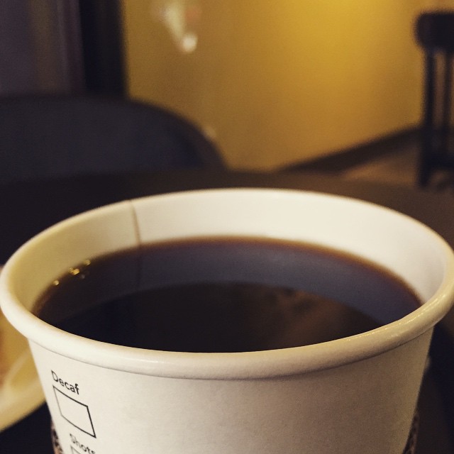 coffee in a paper cup, with a note taped to it, near an empty plate