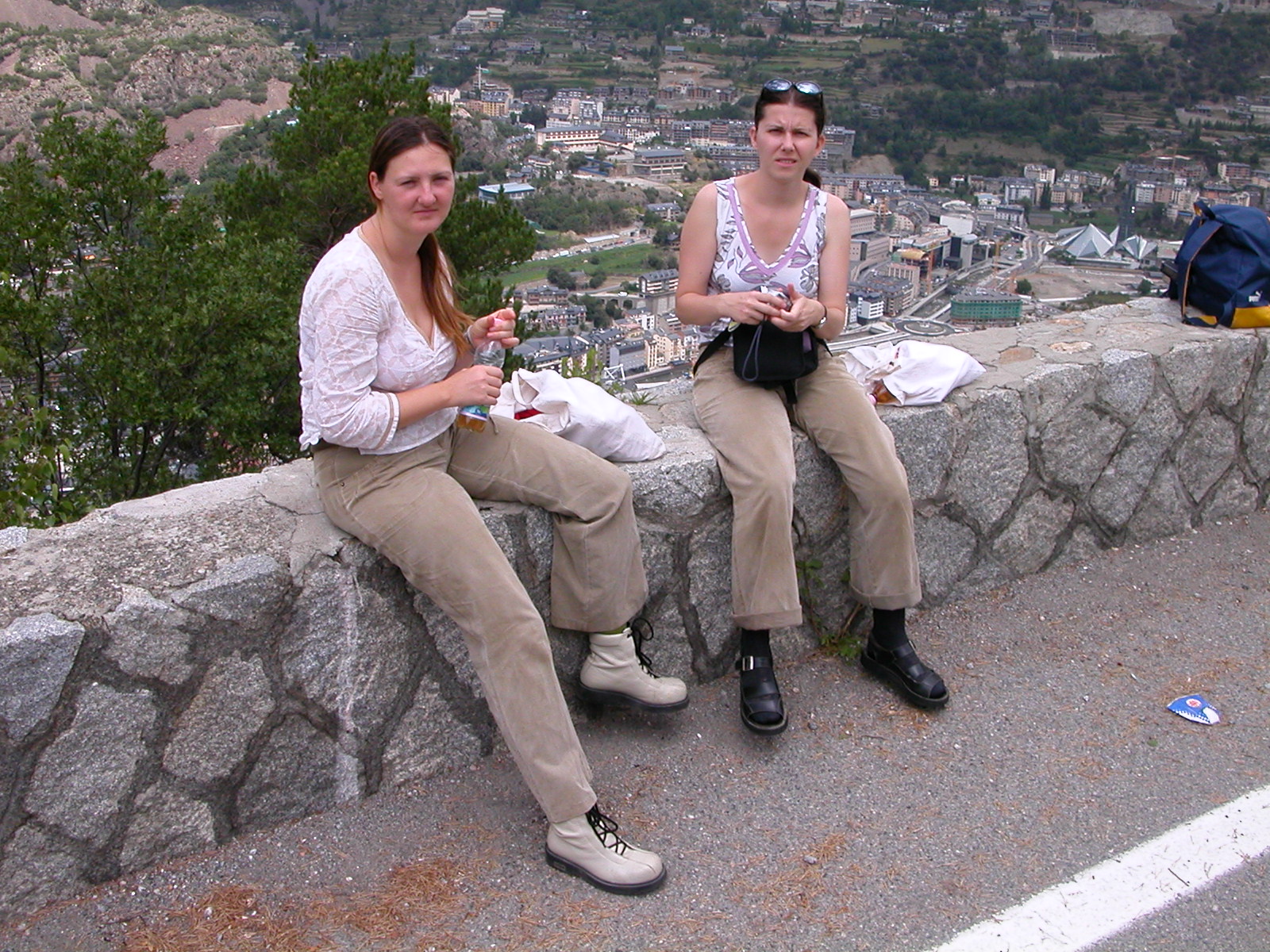 two women are enjoying their time at the park while sitting on a wall