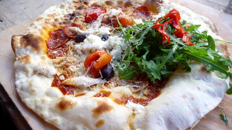 an uncut pizza with arugula, black olives and tomatoes