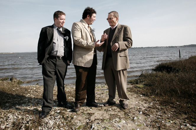 two men stand together and talk on the shore