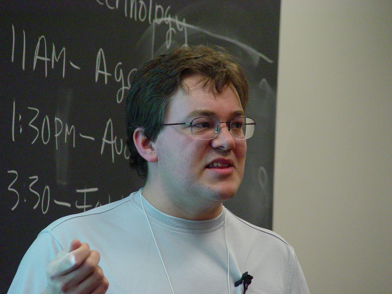 a man with glasses pointing to the side of a blackboard