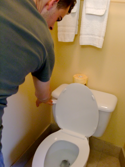 there is a man standing over a white toilet
