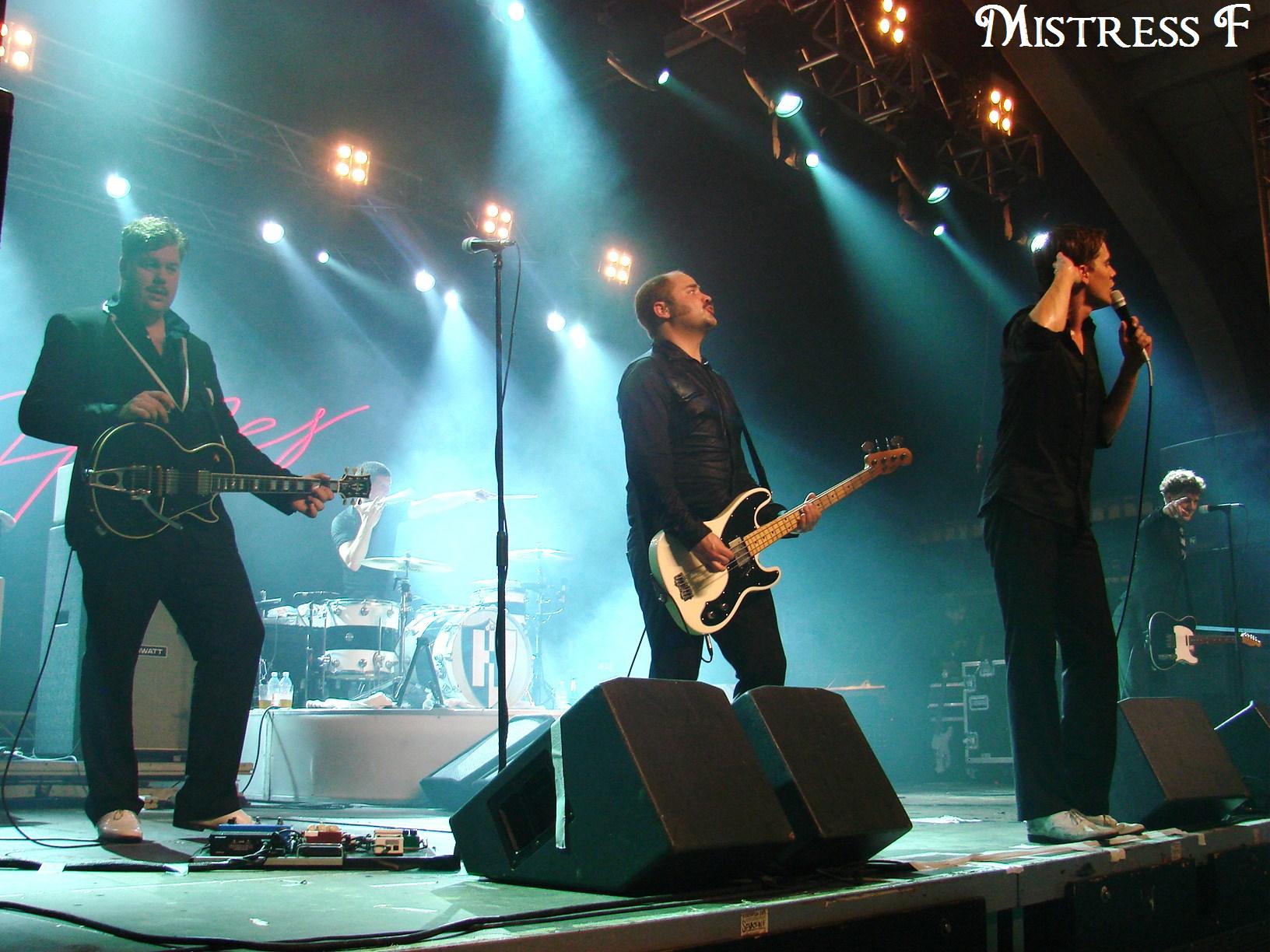 five men on stage with microphones and a guitar