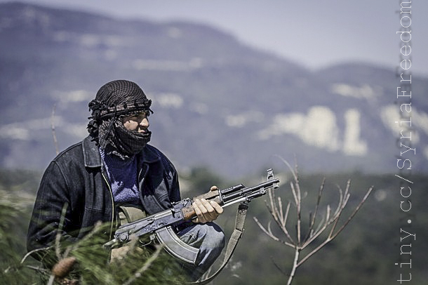 man holding a rifle standing in front of a mountain