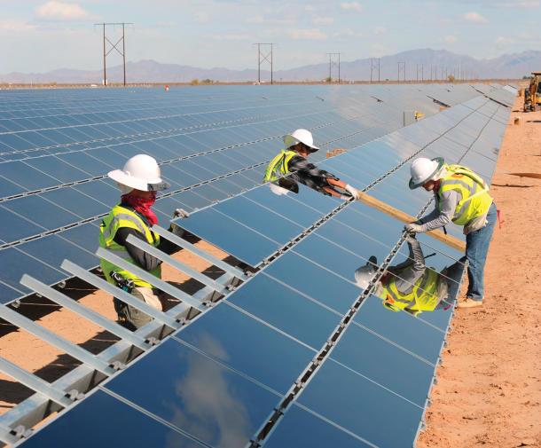workers wearing hard hats install solar panels on top of a large construction area