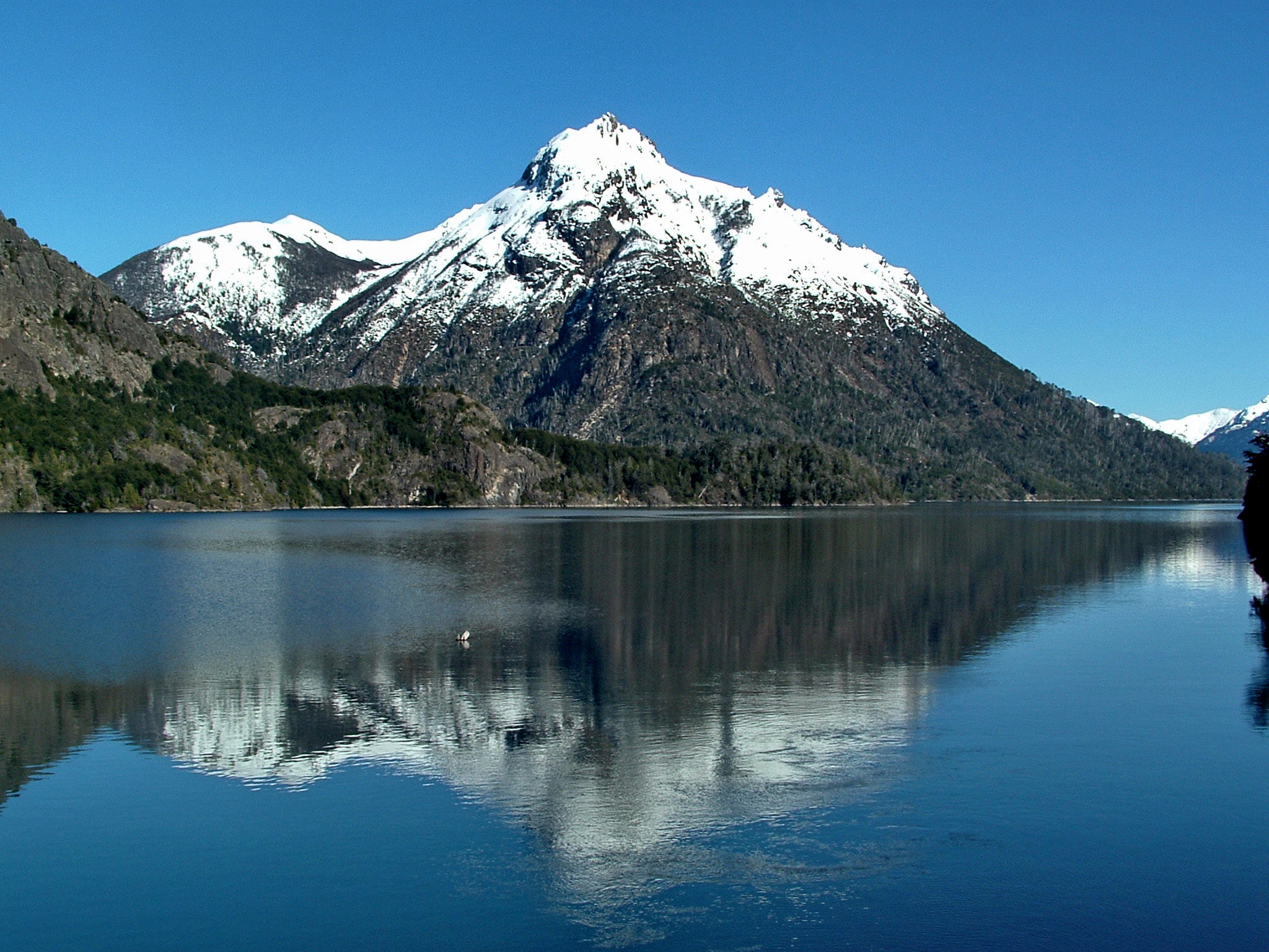 a snow capped mountain on top of a mountain range over water