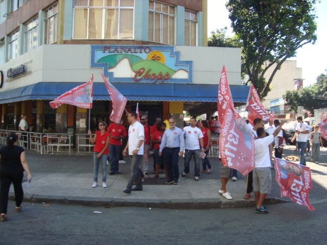 a group of people walking along a sidewalk holding pink and red flags