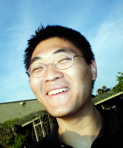 an asian man wearing glasses, in front of a blue sky