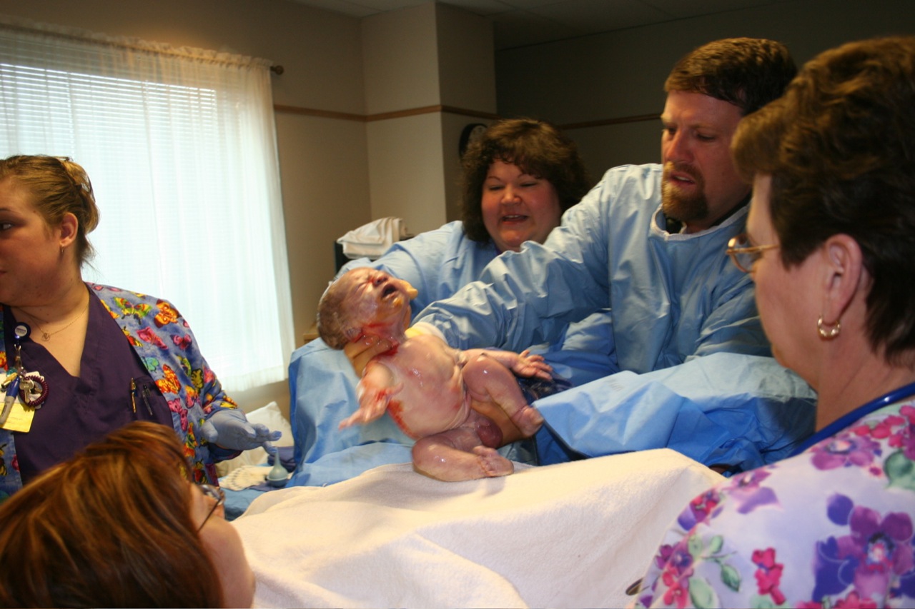 four people in scrubs around a baby being held by a hospital worker