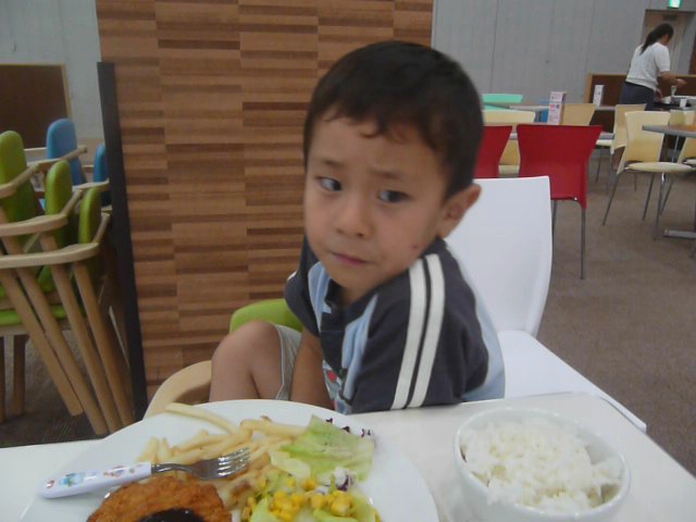 small boy sitting at table with food on plate and paper napkin