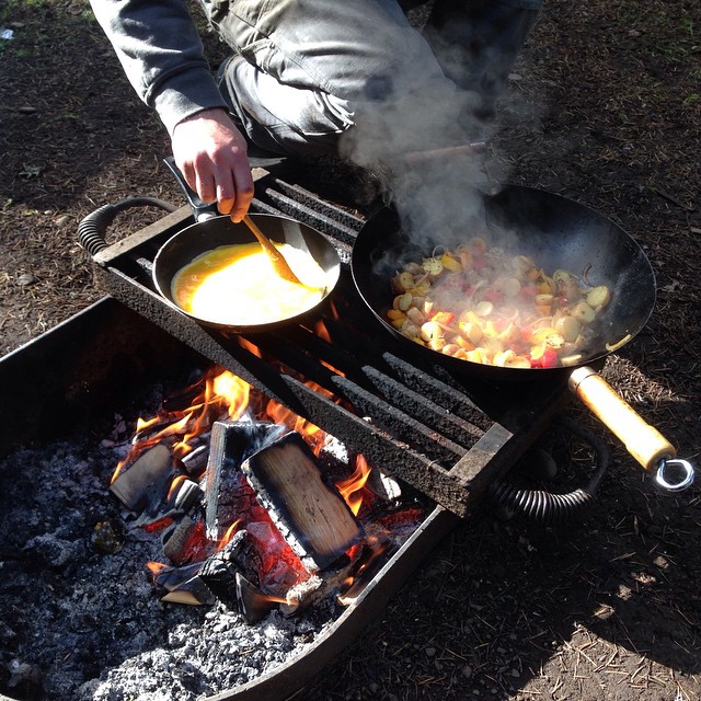 man cooking  food over a campfire while he holds tongs