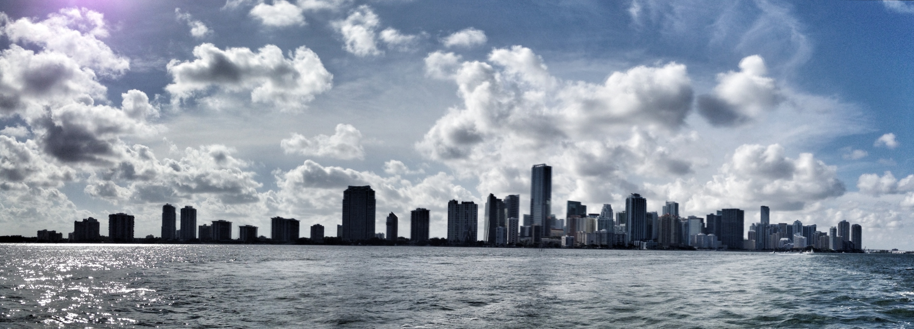 a city skyline seen through the water under a cloudy blue sky