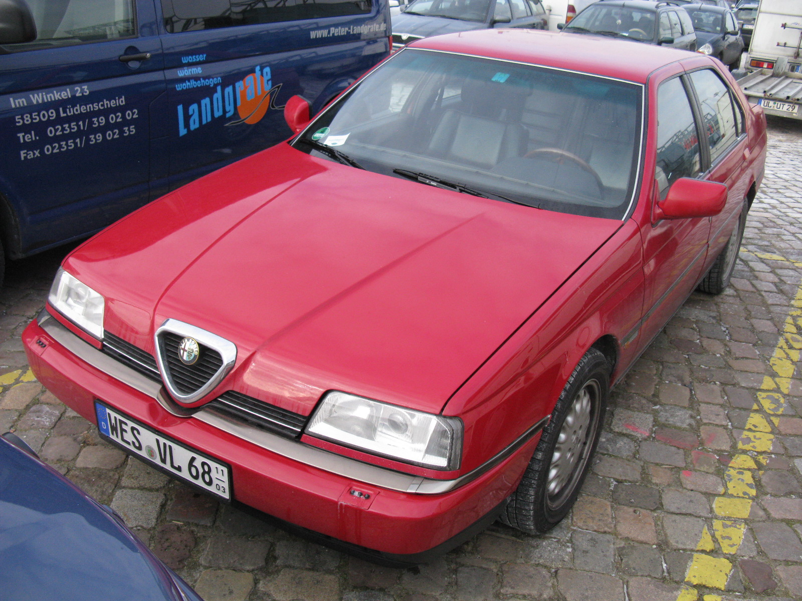 red car sitting next to blue cars on the pavement