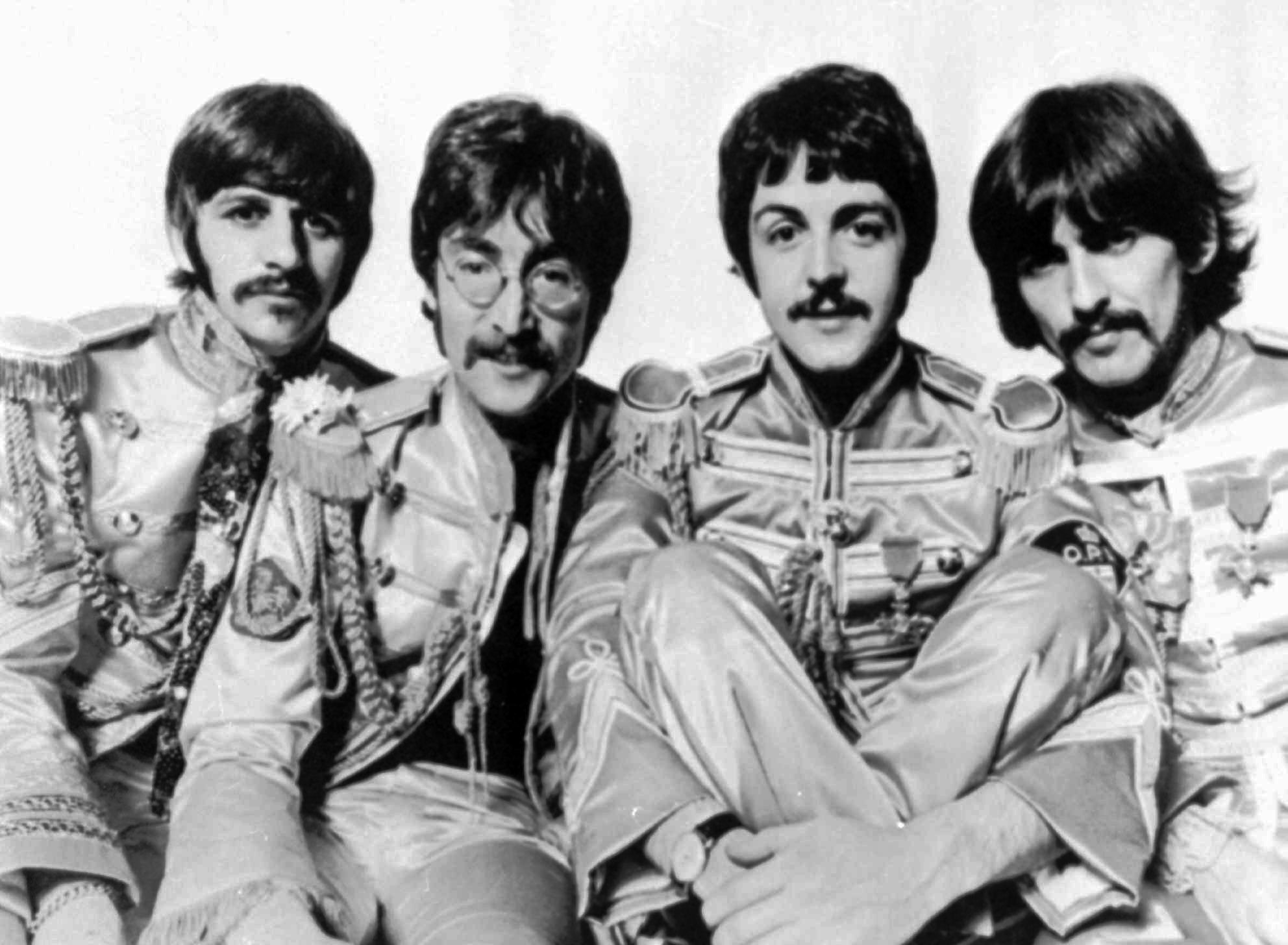 four men are sitting on a bed dressed in different styles of clothing