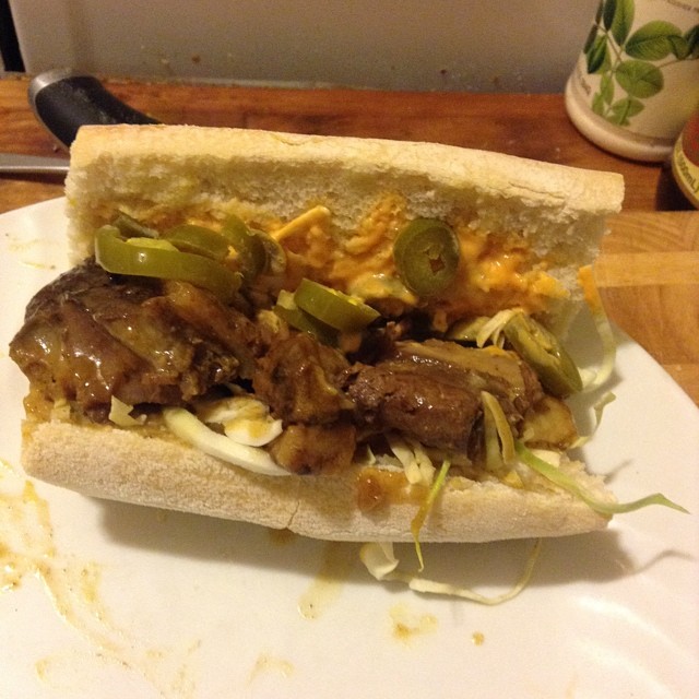 a sandwich of beef, onions and peppers sits on a  board
