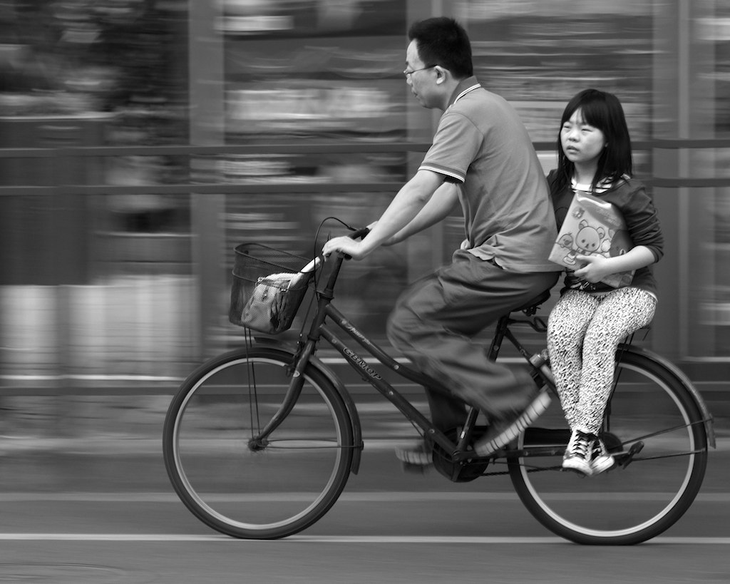 a man riding on the back of a bike while carrying a small girl