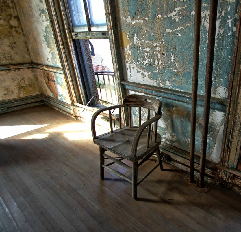 a wooden chair with a broken arm rest against a door